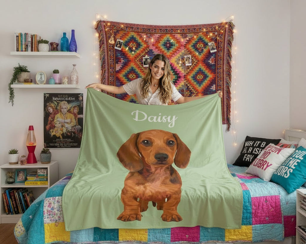 Woman holding a green blanket with a dachshund design and 'Daisy' text in a bedroom setting.