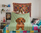 Woman holding a green blanket with a dachshund design and 'Daisy' text in a bedroom setting.