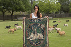 Woman holding a decorative blanket with a dog design in a park with dogs in the background