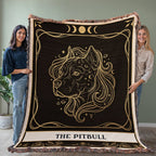 Two people holding a decorative blanket with a pitbull design against a plain wall.