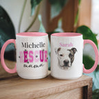 Two mugs with pink handles on a wooden surface, one featuring text and the other with a dog's face.