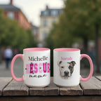 Two mugs with pink handles on a wooden surface, one featuring text and the other with a dog's face.