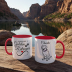 Two mugs with red interior and handles on a wooden surface with a scenic background of a lake and mountains.